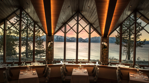 Elegant restaurant interior with large windows showcasing a scenic lake and mountains at sunset.