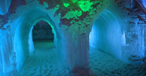Two icy arches illuminated with blue and green light, creating a mystical atmosphere in a snow cave.