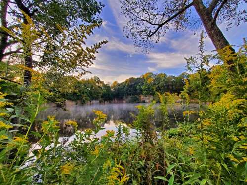 A serene lake surrounded by lush greenery and mist, under a colorful sky at dusk.