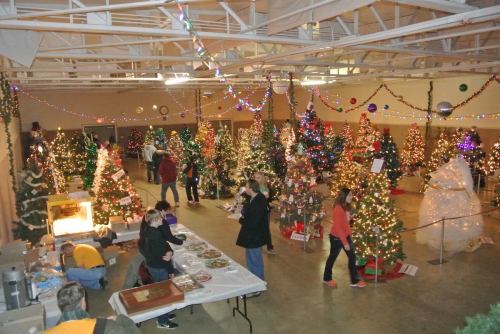 A festive indoor space filled with decorated Christmas trees and people enjoying holiday activities.