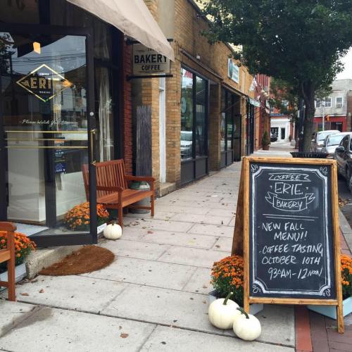 A bakery storefront with a sign advertising a new fall menu and coffee tasting event, surrounded by autumn decorations.