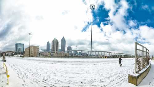 A snowy urban landscape with tall buildings and a person walking, under a cloudy blue sky.