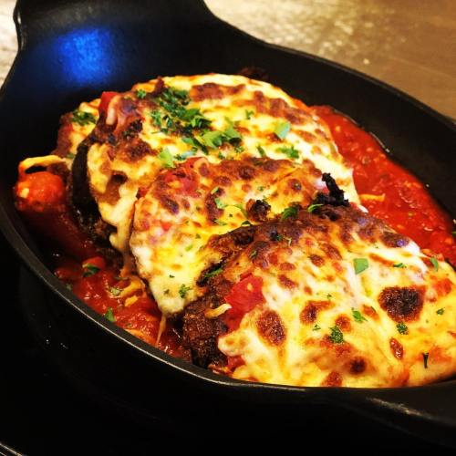 A sizzling skillet with three cheesy meat patties on a bed of marinara sauce, garnished with parsley.