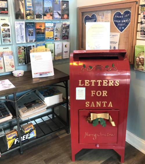 A red mailbox labeled "Letters for Santa" sits beside a display of brochures and a sign in a cozy setting.