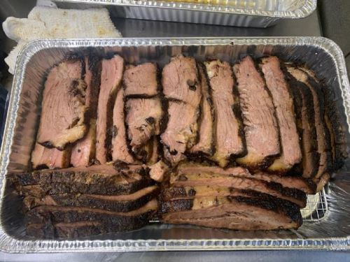 Sliced smoked brisket arranged in a foil tray, showcasing a mix of tender meat and crispy edges.