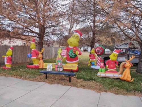 Colorful holiday decorations featuring the Grinch, his dog Max, and festive gifts in a yard with trees.