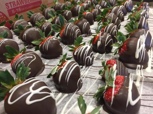 A close-up of chocolate-covered strawberries arranged neatly, drizzled with white chocolate and garnished with green leaves.