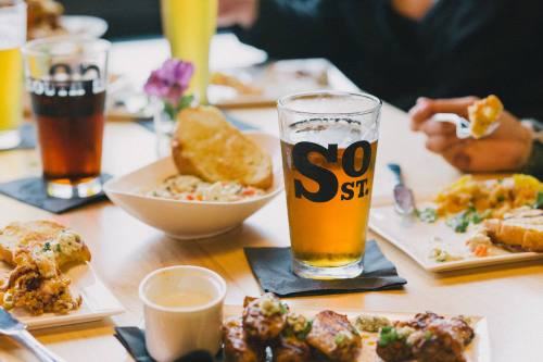 A table with various dishes, including salad, wings, and drinks, featuring a glass of beer prominently in the center.