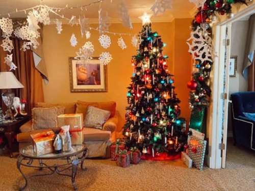 Cozy living room decorated for Christmas, featuring a colorful tree, presents, and festive snowflake decorations.