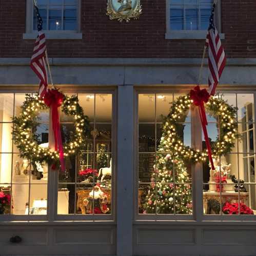 Festively decorated storefront with wreaths, lights, and a Christmas tree, adorned with red ribbons and holiday decor.