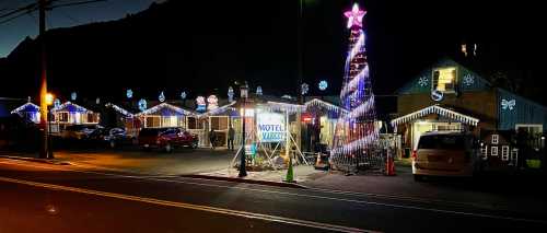 A festive scene of a motel decorated with colorful lights and a large illuminated Christmas tree at night.