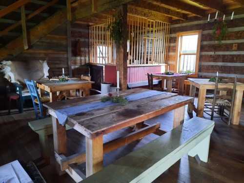 Interior of a rustic cabin with wooden tables and benches, featuring a staircase and a cozy, inviting atmosphere.