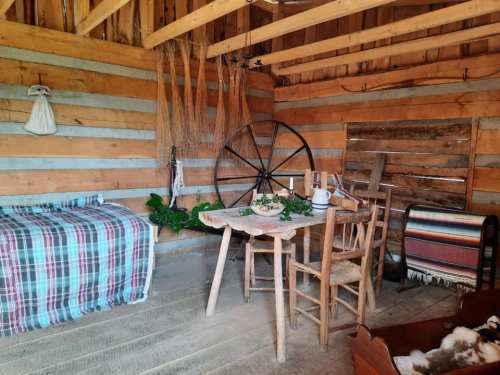 A rustic interior featuring a wooden table, chairs, a plaid blanket, and traditional decor in a cozy, warm setting.
