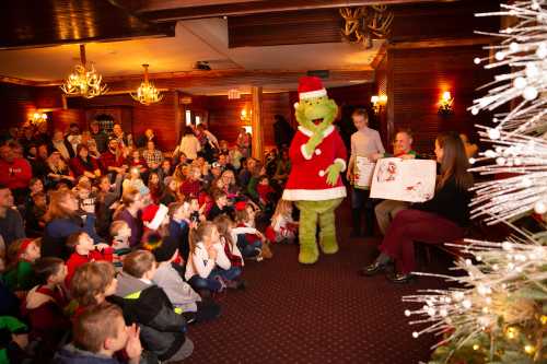 A festive gathering with children in holiday attire, as the Grinch entertains while a storyteller reads.