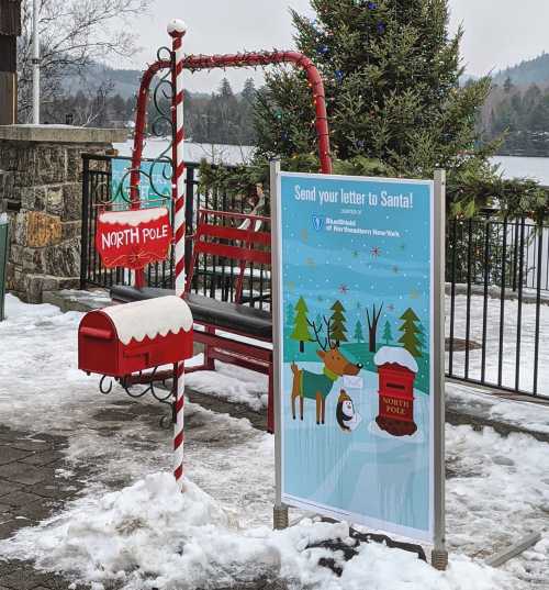 A festive mailbox labeled "North Pole" with a sign inviting letters to Santa, surrounded by snow and holiday decorations.