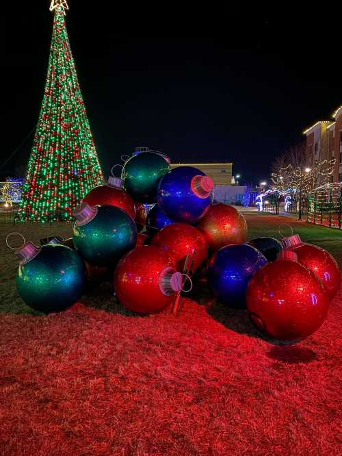 A colorful pile of large Christmas ornaments in red and blue, with a lit tree in the background at night.