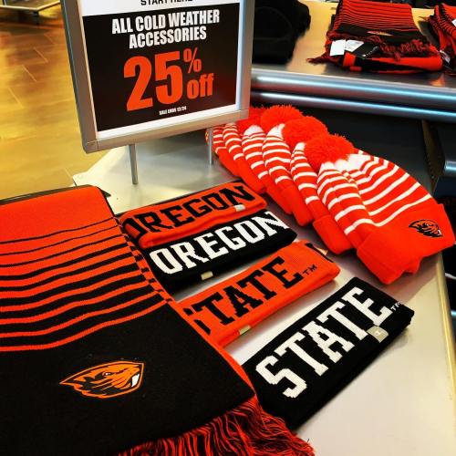 Display of cold weather accessories, including scarves and beanies, with a sign indicating 25% off.