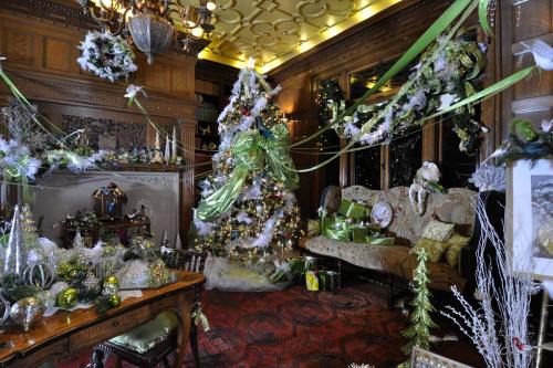 A festive room decorated for Christmas, featuring a green-themed tree, garlands, and elegant furnishings.