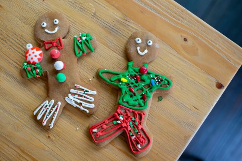 Two decorated gingerbread cookies on a wooden table, one in green and red, the other in brown with festive icing.