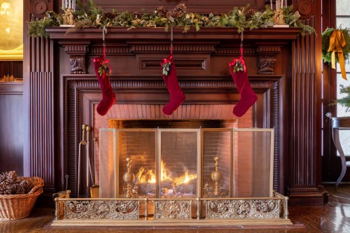 A cozy fireplace adorned with stockings, festive greenery, and a warm fire, creating a holiday atmosphere.