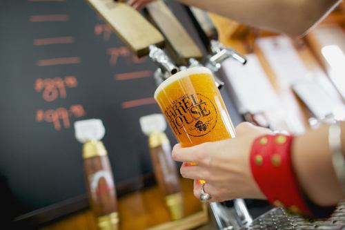 A hand pours a golden beer into a glass at a bar, with a chalkboard menu in the background.