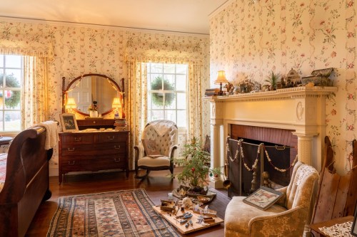 Cozy vintage bedroom with floral wallpaper, a fireplace, and a decorated Christmas tree. Warm, inviting atmosphere.