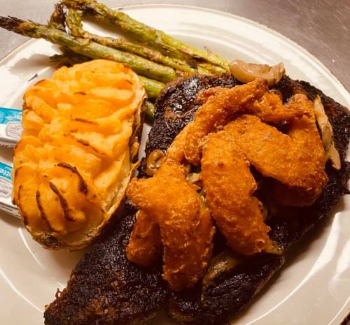 A plate featuring grilled asparagus, a baked potato, and a blackened fish fillet topped with crispy shrimp.