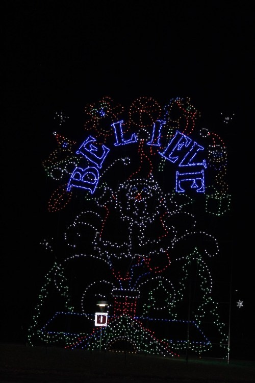 Colorful holiday lights display featuring the word "BELIEVE" and festive decorations against a dark night sky.