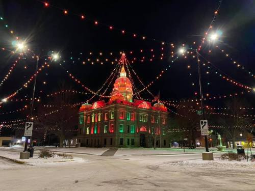 A brightly lit building adorned with red and green lights, surrounded by festive string lights at night. Snow on the ground.