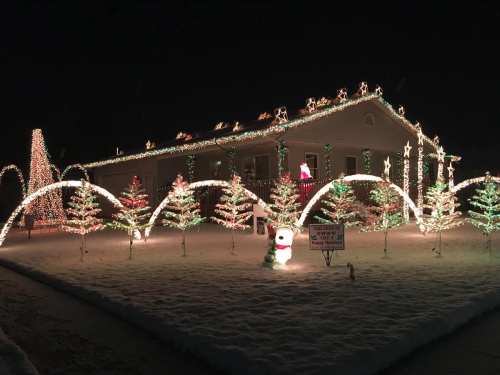 A house decorated with colorful Christmas lights, featuring illuminated trees and a snowman in a snowy yard.