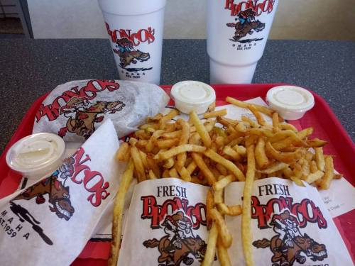 A red tray with two large drinks, fries, and two wrapped sandwiches from Bronco's, featuring their logo.