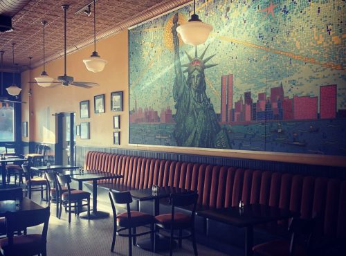 A cozy restaurant interior featuring a mosaic of the Statue of Liberty on the wall and red upholstered seating.