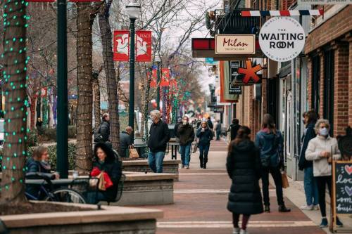A busy street scene with people walking, shops, and festive decorations, some wearing masks during winter.