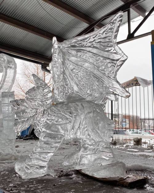 A detailed ice sculpture of a dragon with wings, set in a snowy outdoor environment.