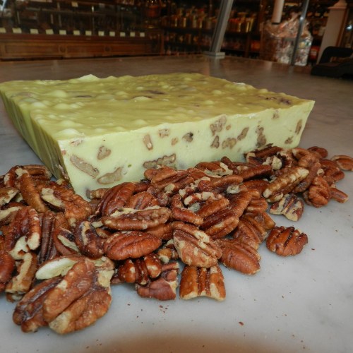A large block of creamy fudge with nuts, surrounded by a pile of pecans on a marble surface.
