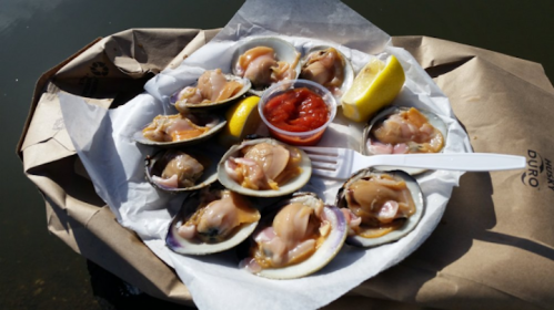 A plate of freshly served clams with lemon wedges and a side of ketchup, resting on a paper surface.