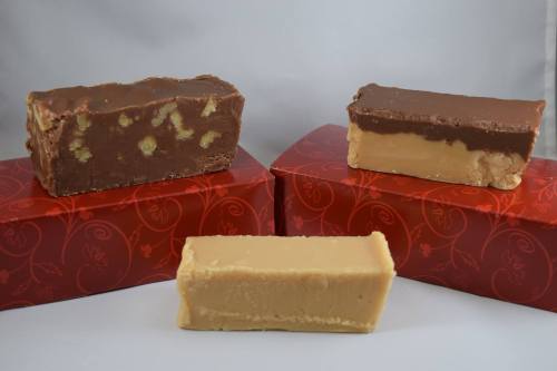 Three pieces of fudge: one chocolate with nuts, one chocolate layer, and one creamy beige fudge, displayed on red boxes.