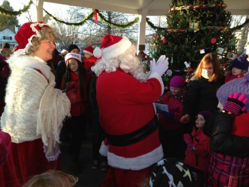 Santa and Mrs. Claus greet children at a festive holiday event near a decorated Christmas tree.