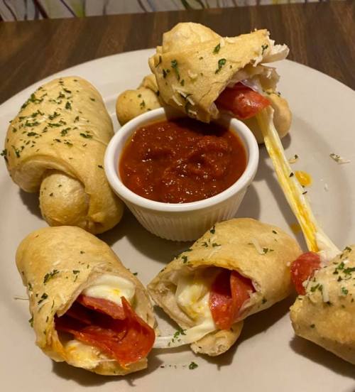 A plate of cheesy pepperoni rolls with marinara sauce, garnished with herbs.