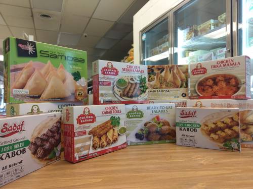 A variety of frozen food products, including samosas, kababs, and chicken tikka masala, displayed on a wooden table.
