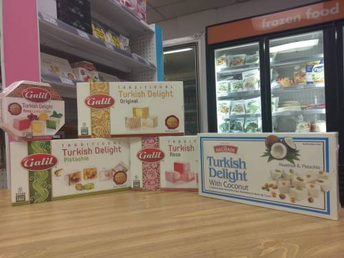 A display of various Turkish Delight boxes, including flavors like pistachio, rose, and coconut, on a wooden table.