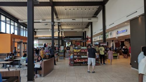 A busy indoor food court with various shops, including Starbucks, and people seated and standing around.