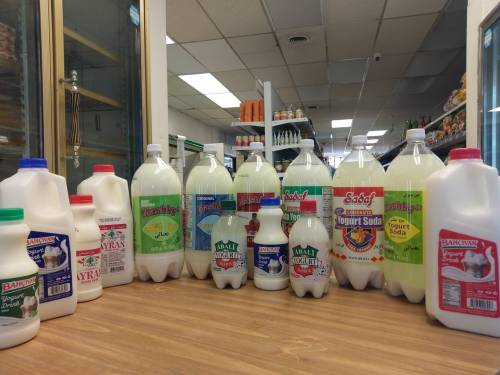 A variety of milk and yogurt soda bottles displayed on a wooden table in a grocery store aisle.