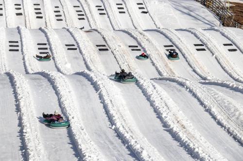 People sledding down a snowy hill on inflatable tubes, with multiple lanes and snow-covered tracks.