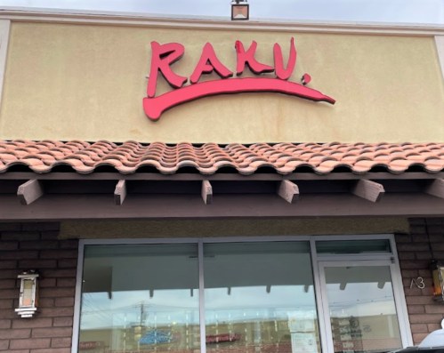 Sign for "RAKU" above a restaurant entrance with a tiled roof and large windows.