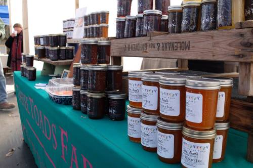 A display of jars filled with various jams and jellies on a green table at a market.