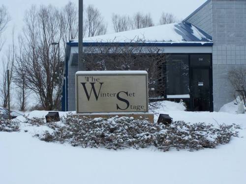 Sign for "The Winterset Stage" in front of a building, surrounded by snow and bare trees.