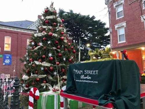 A decorated Christmas tree with red ornaments stands beside a table draped in green, promoting Main Street Berlin.