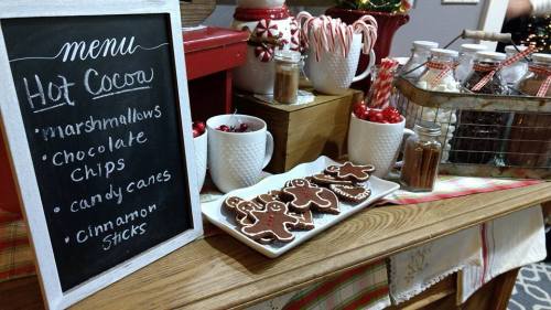 A festive hot cocoa station with a chalkboard menu, cookies, candy canes, and jars of toppings.