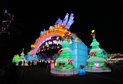 Colorful illuminated archway with Christmas trees and festive decorations, glowing brightly against a night sky.
